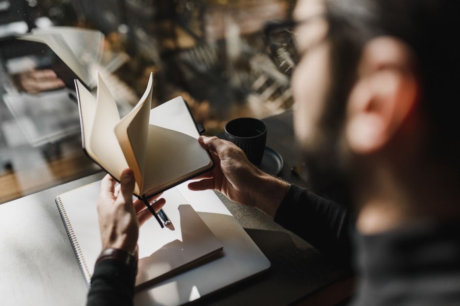 A person flips through a notebook while seated by a window, enjoying a cozy ambiance.