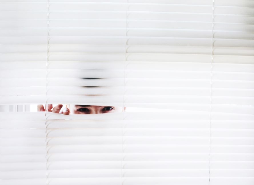 A person peeks through white blinds, creating an intriguing sense of curiosity.