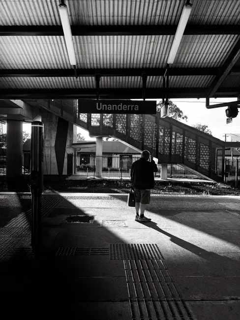 A person standing at Unanderra train station, captured in black and white, creating a moody and dramatic effect.