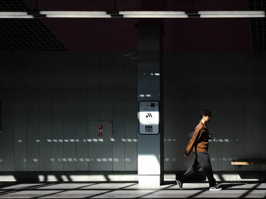 A person walks through a sunlit subway station, casting dynamic shadows.