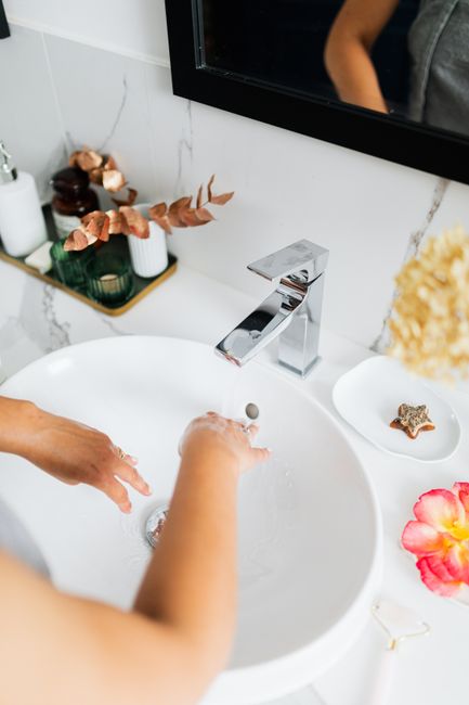 A person washing hands in a stylish white ceramic sink with modern fixtures and decor.