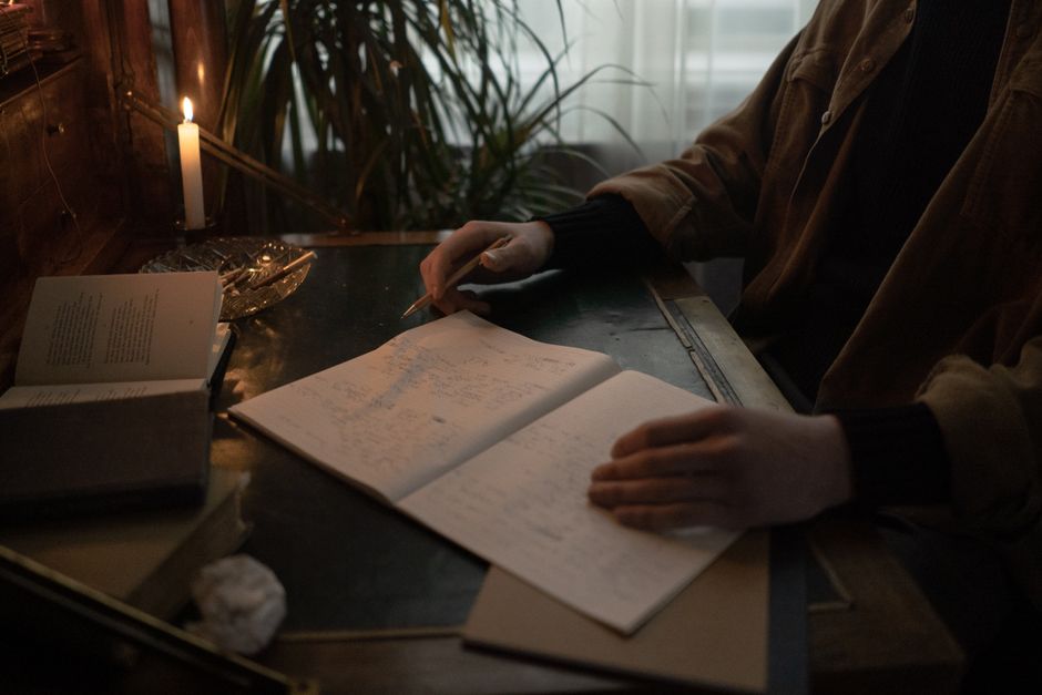 Hypomanie : quand l’énergie, le sommeil et l’humeur accélèrent A person writes in a dimly lit room, surrounded by open books and candlelight, creating a moody study atmosphere.