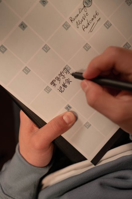 A person writing a reminder in a calendar with a pen.
