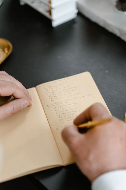 A person writing in a notebook with a pencil, focusing on note-taking.