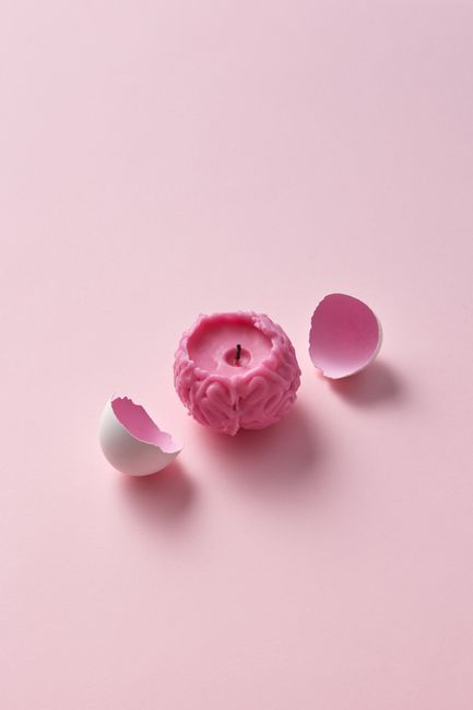 A pink brain-shaped candle with eggshells on a light pink background, offering artistic minimalism.