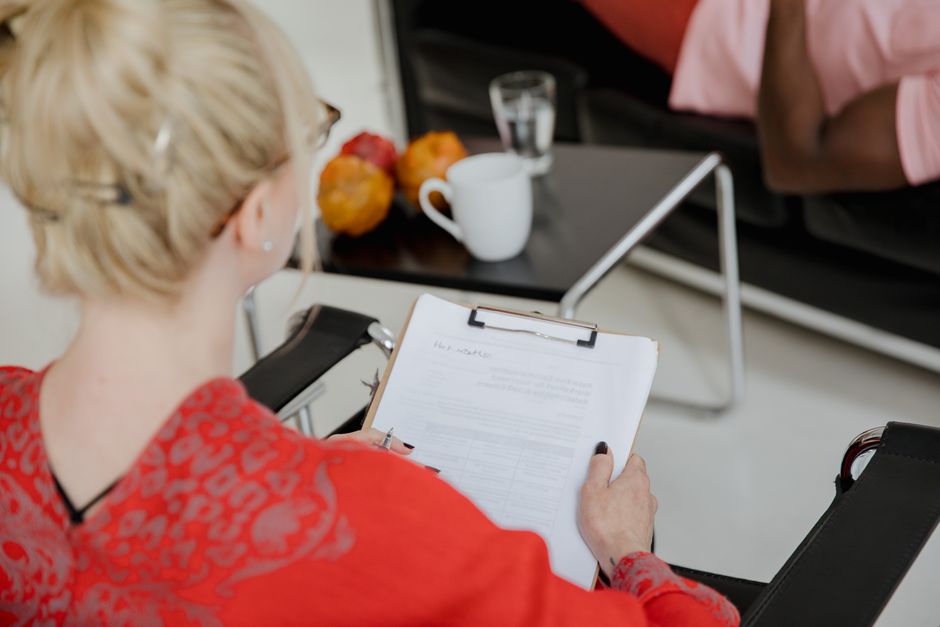 A psychologist takes notes during a therapy session with a client, indoors.