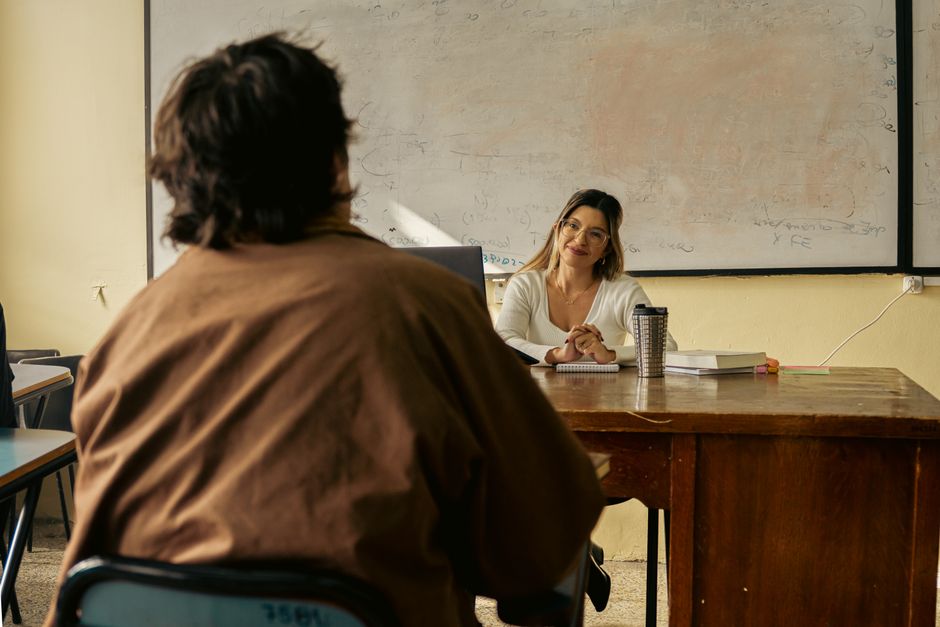 A teacher engages with a student in a university classroom setting, fostering learning.