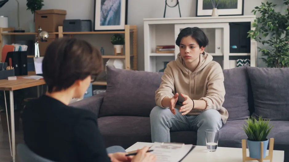 Santé mentale des jeunes : comprendre la crise, agir sans raccourci A teenager discusses with a therapist during a counseling session in a modern office setting.