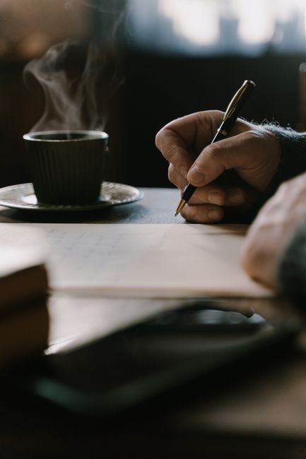 A warm scene of a person writing a note with a steaming coffee cup nearby.