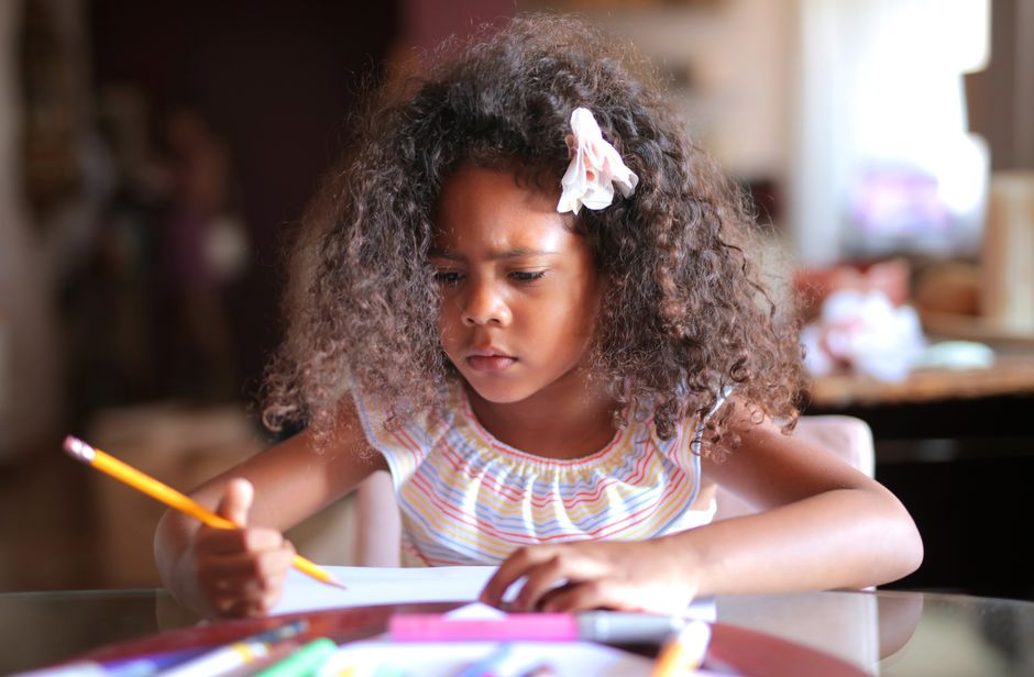 African American child focused on homework, writing with a pencil indoors.