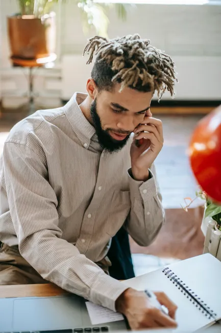 African American man multitasking, talking on phone and writing notes indoors.