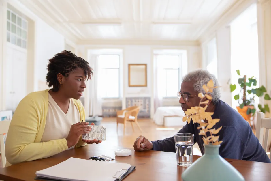 Schizophrénie résistante aux traitements : l’adhésion ne se résume pas aux médicaments An elderly man sits with a caregiver discussing medication at a table in a bright room.