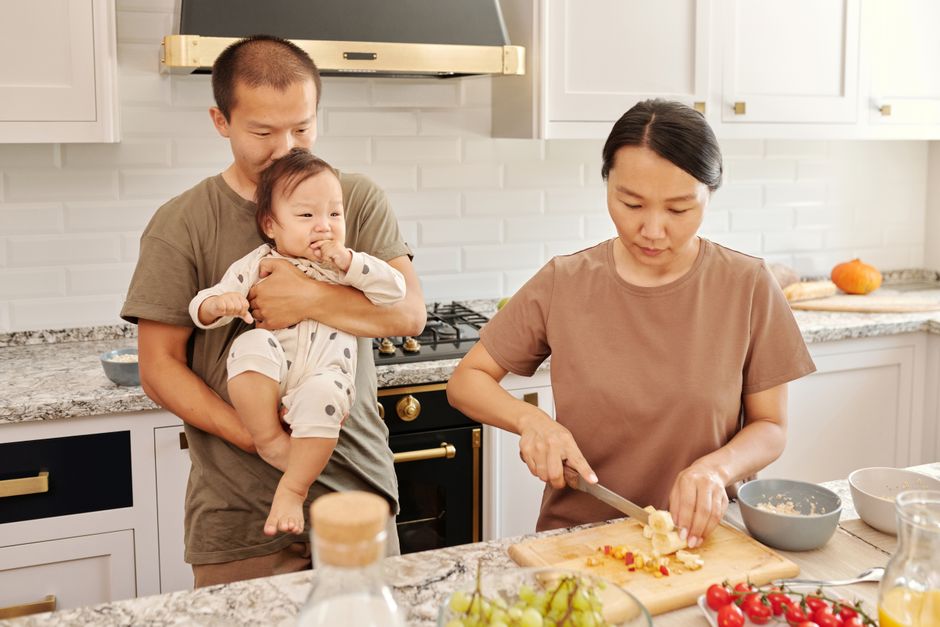 Asian parents with toddler cooking together, sharing a moment in the kitchen.