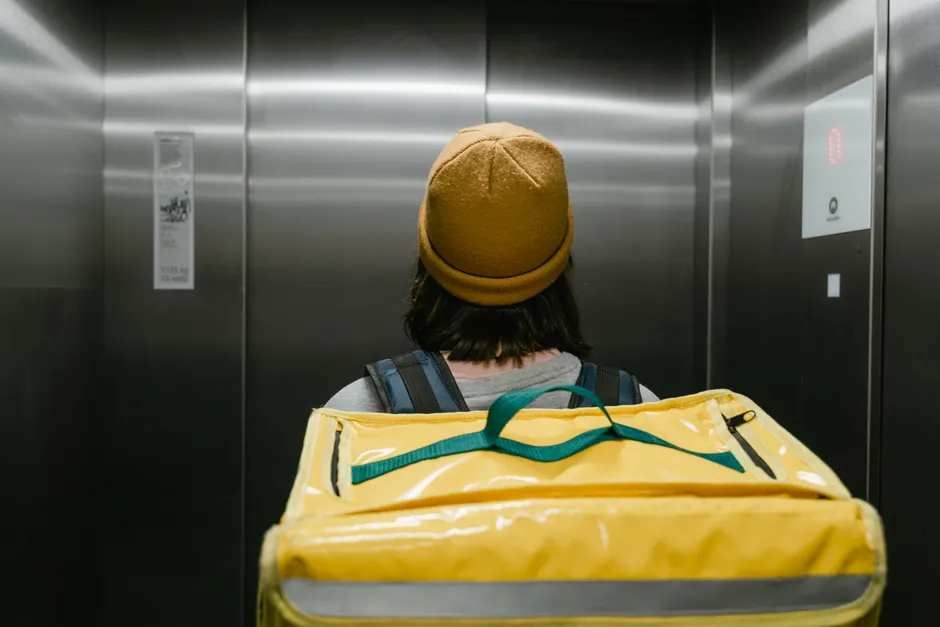 Back view of a delivery person with a yellow thermal bag inside an elevator.