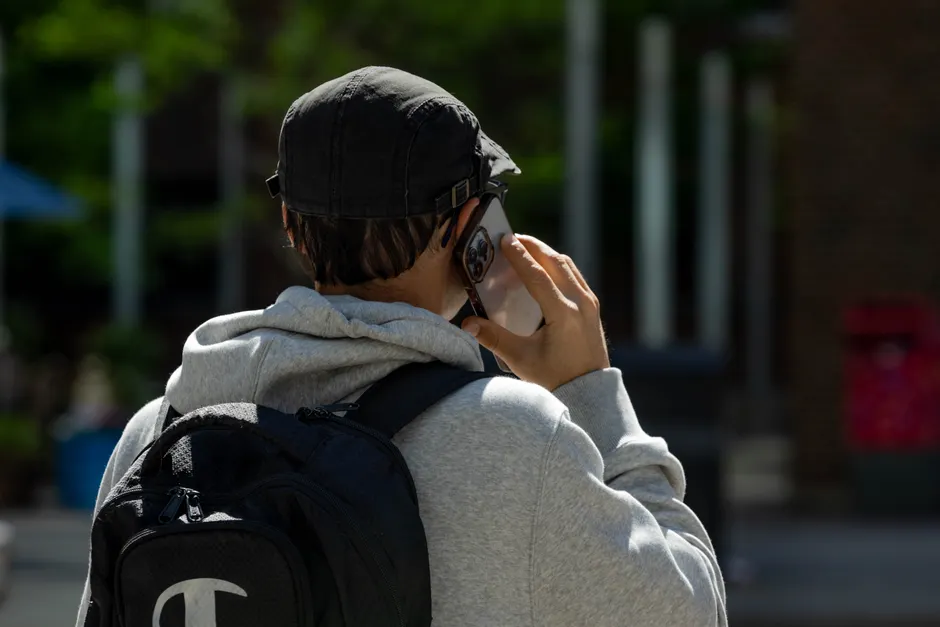 Back view of a man in a cap with a backpack talking on a smartphone outdoors.