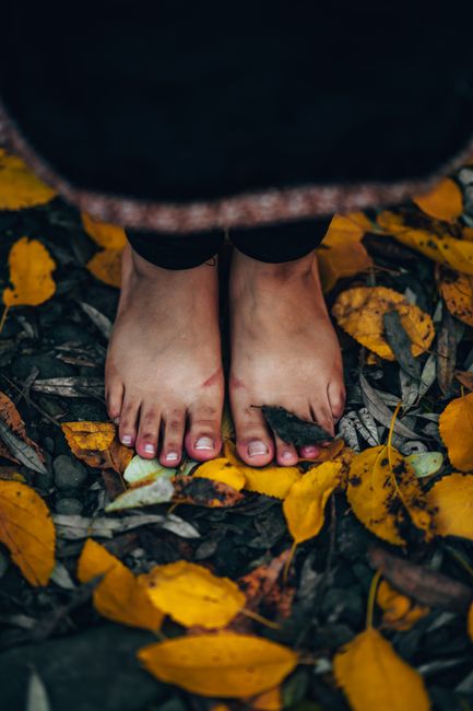 Bare feet standing on colorful autumn leaves on a forest floor.