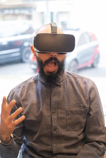 Bearded man with VR headset reacts excitedly indoors, showcasing immersive technology.