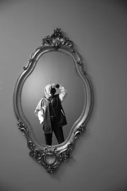 Black and white photo of a hijabi woman taking a selfie in a vintage mirror.