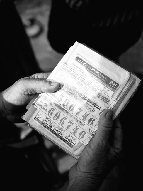 Black and white photo of elderly hands holding Vietnamese lottery tickets, showcasing age and chance.