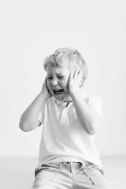 Black and white portrait of a sad child covering ears, expressing frustration.