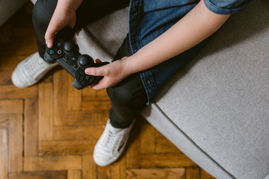 Child holding a game controller while sitting on a sofa, focused on playing a video game.