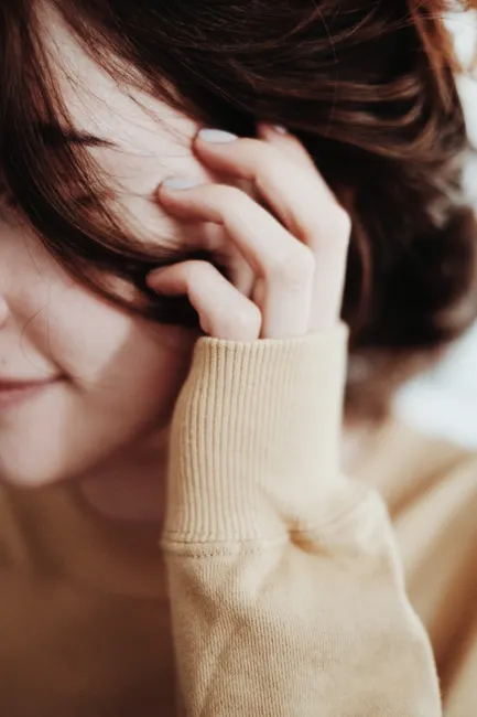 Close-up image of a woman smiling softly, with hand in hair, wearing a cozy sweater.