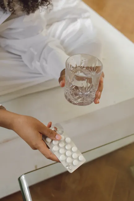 Close-up of a person holding a blister pack of tablets and a glass of water indoors.