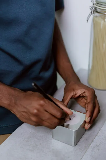 Close-up of a person labeling a metal box in a kitchen, highlighting organization.