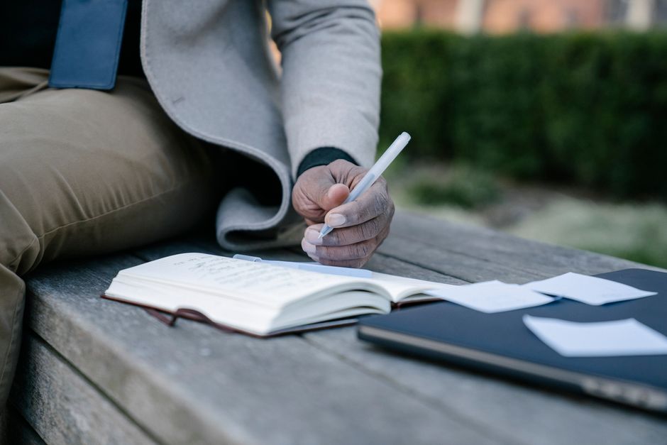 Close-up of a person writing in a notebook on a bench, conveying reflection and creativity outdoors.