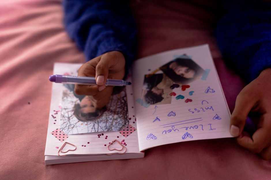 Close-up of a person writing in a personal diary with photographs and decorative elements indoors.