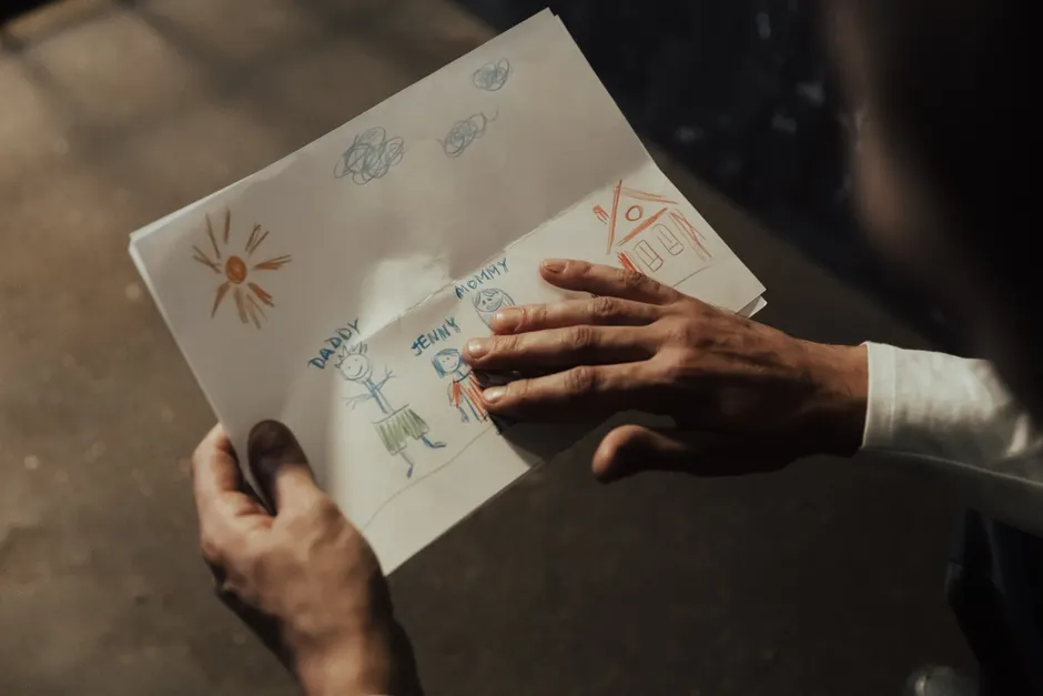 Deuil chez l’enfant : quand la tristesse se cache dans les gestes Close-up of a person's hands holding a child's drawing depicting a family scene.