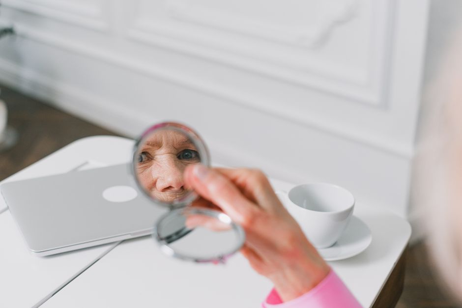 Close-up of a senior woman holding a pocket mirror, reflecting her face indoors.