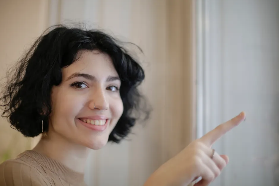 Close-up of a smiling woman with short hair and nose ring pointing outside.
