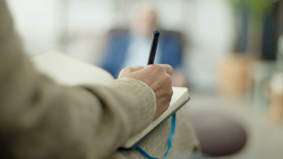 Close-up of an adult writing in a notebook with a pen, depth of field effect.