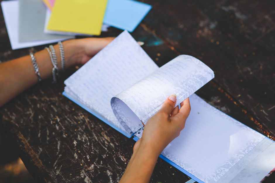 Close-up of hands flipping through a notebook on a worn wooden table. Outdoors setting, relaxed atmosphere.