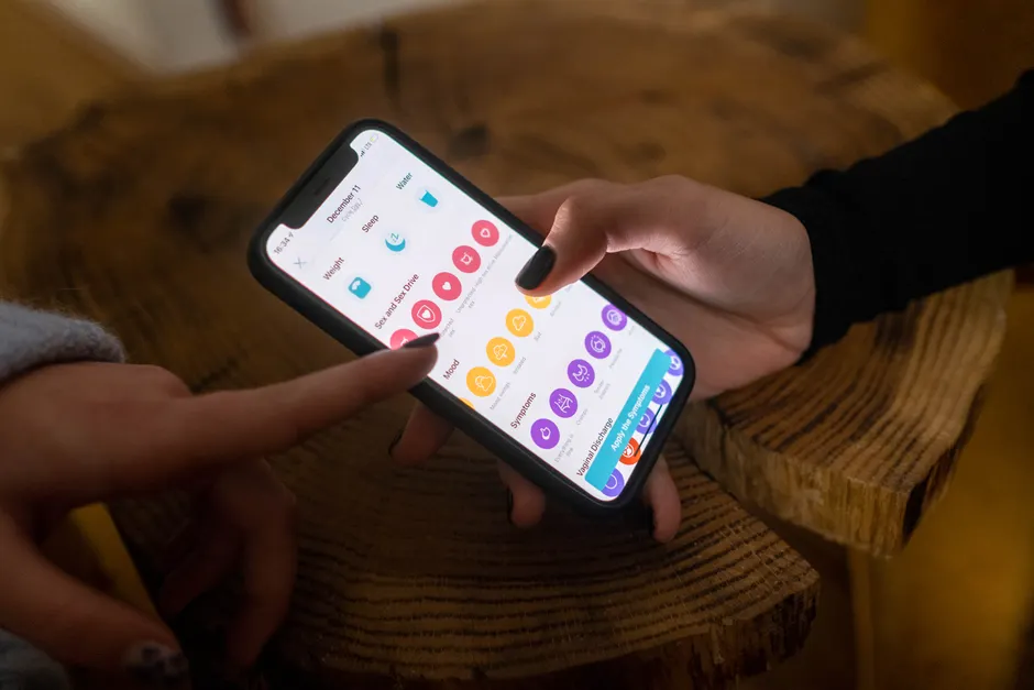 Close-up of hands using a fertility tracking app on a smartphone indoors.