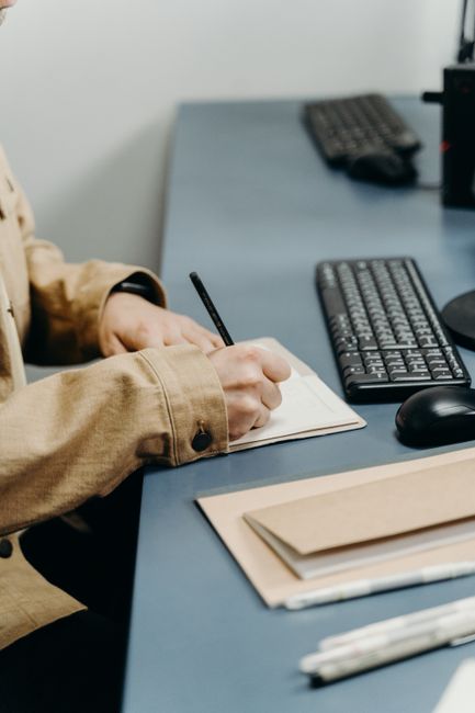 Close-up of hands writing in a notebook on an office desk with keyboard.