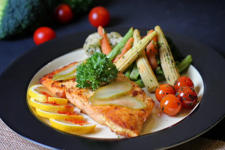 Colorful plate of grilled fish garnished with lemon, pickles, and fresh vegetables. Perfect for healthy meal inspiration.