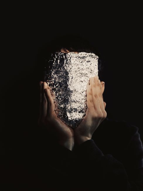 Conceptual image of a person holding a foil sheet over face, obscuring identity.