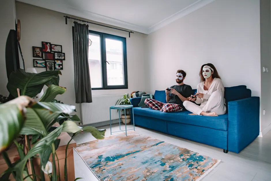 Couple enjoying video games on a sofa while applying relaxing face masks at home.