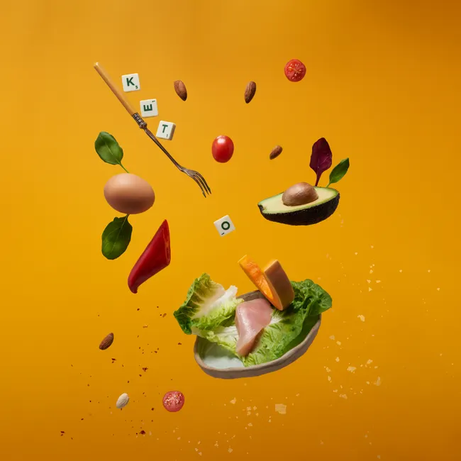 Creative composition of ketogenic diet foods and letters floating on a vibrant background.