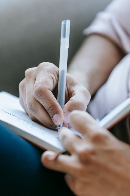 Crop anonymous person taking notes in diary placed on laps in light room
