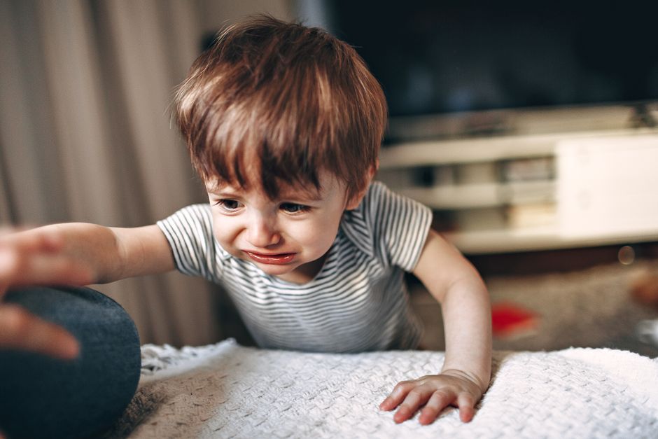Crop unrecognizable parent helping unhappy child to get on comfortable sofa in light living room with modern TV in apartment