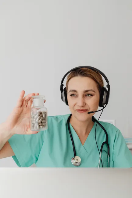 Female doctor with headset holding pill bottle. Telemedicine concept.