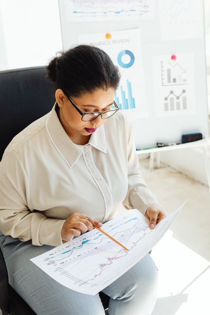 Focused businesswoman reviewing financial documents with charts and graphs in a modern office setting.
