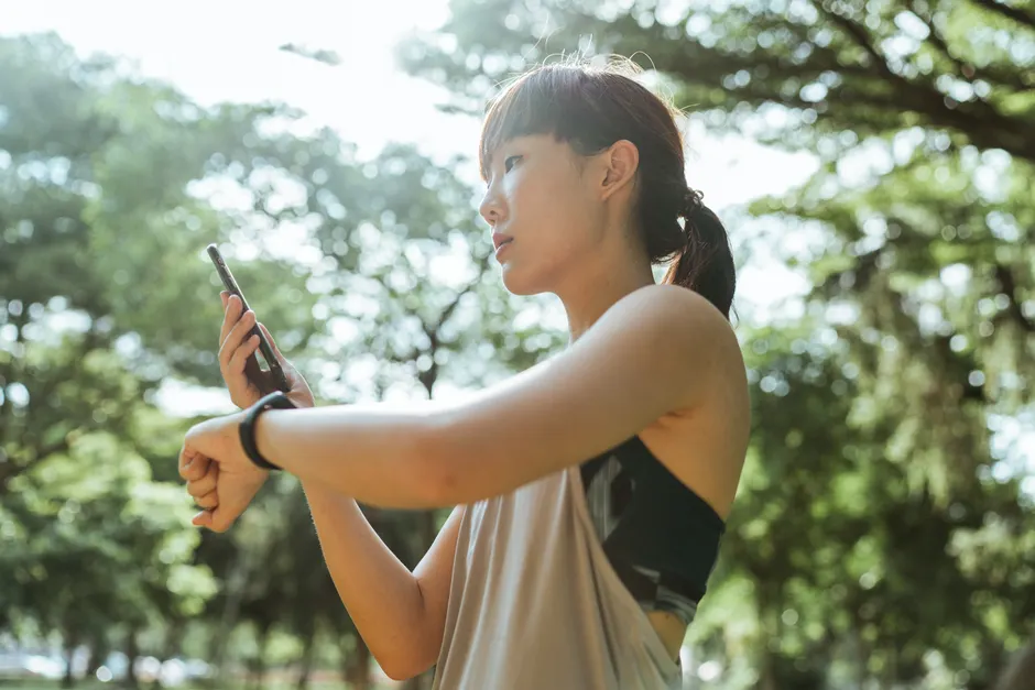 From above of young ethnic female in sportswear using smartphone and smart watch for restoring after exercising