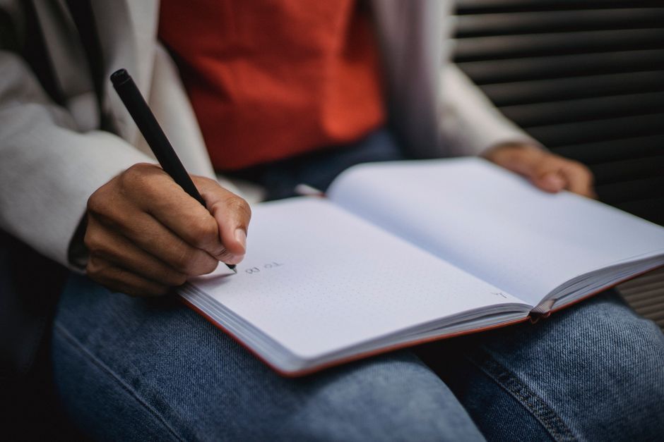 Hand holding pen writing in an open notebook, indicating study or journaling.