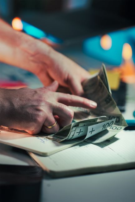 Hands counting cash over a notepad, with euro banknotes, in a busy workspace setting.