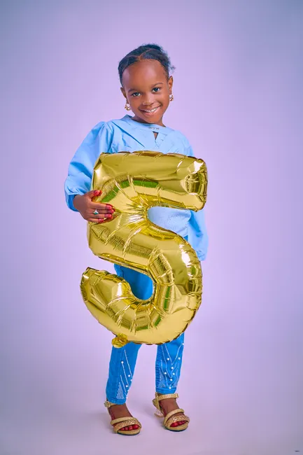 Happy child holding a gold number five balloon, celebrating a birthday indoors.