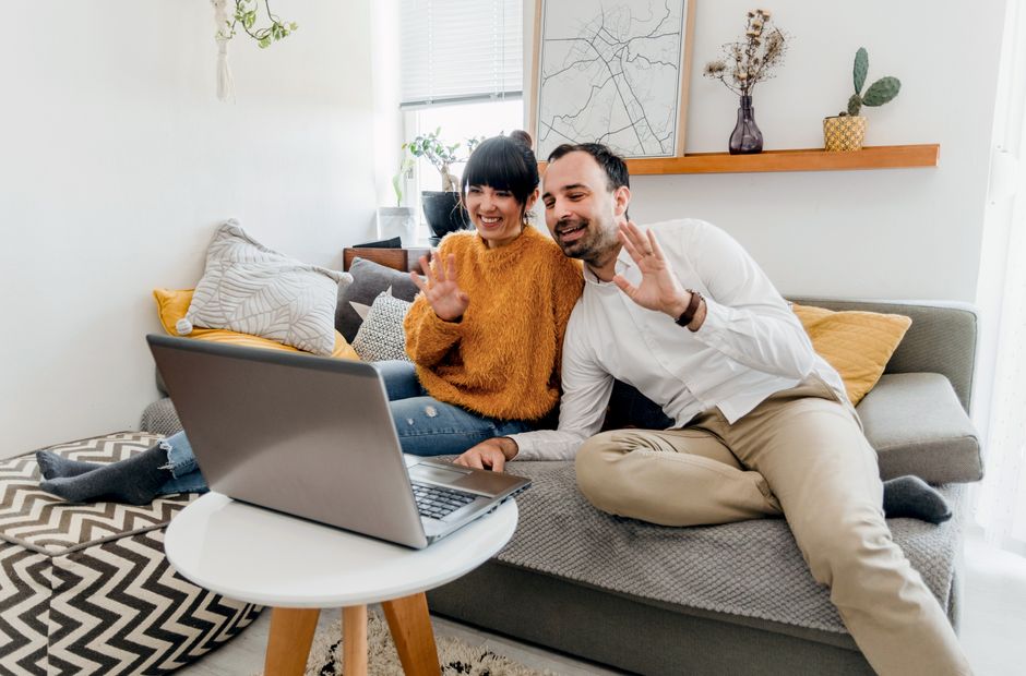 Thérapie de couple en ligne : ce que la visioconférence change vraiment Happy couple sitting on couch, using laptop for a video call in a stylish living room.